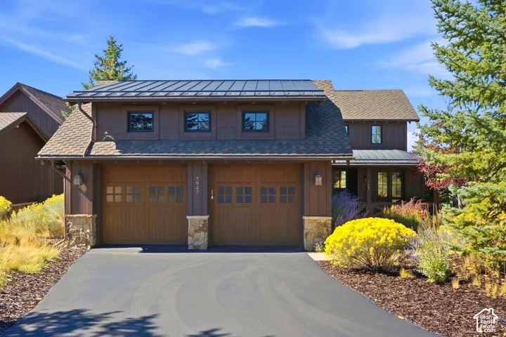 Two-car garage exterior featuring a metal roof, cedar-style siding, stone veneer accents, and multi-pane carriage-style garage doors