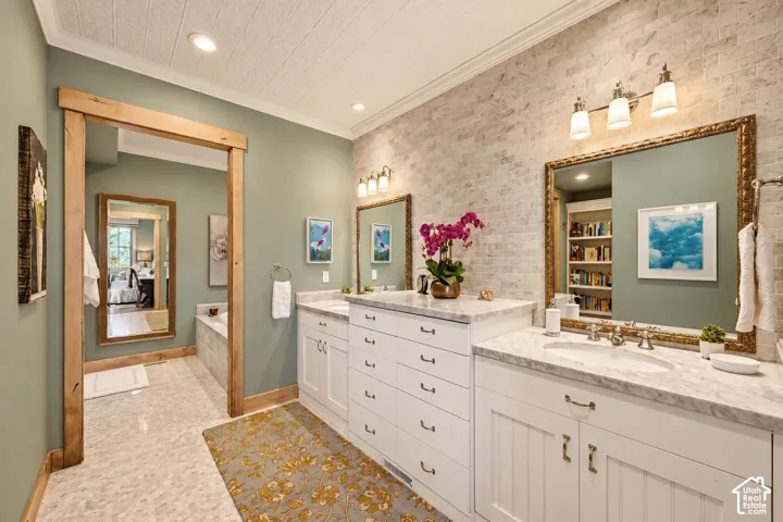 Dual vanity featuring white cabinetry, stone-surface countertops, textured stone wall cladding, and integrated rectangular mirrors with metallic framing