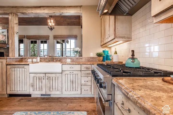 Kitchen featuring stone countertops, white farmhouse sink, subway tile backsplash, custom wood-finish cabinetry, and professional-grade stainless steel range