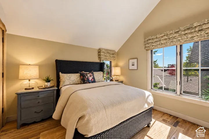 Vaulted ceiling featuring neutral wall paint, multi-pane windows, and wood-finish flooring