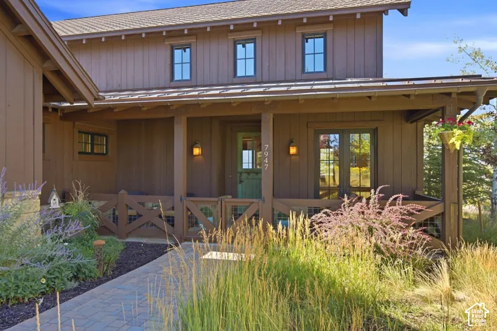 Exterior featuring board-and-batten siding, a covered porch with X-brace railing, metal roofing, stone accents, and a paver walkway