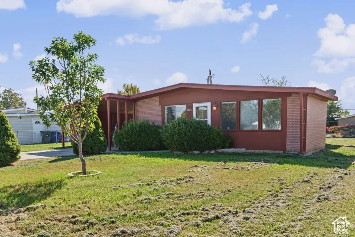 Single-story residence featuring a brick facade, low-pitched roofline, large picture windows, and an attached carport