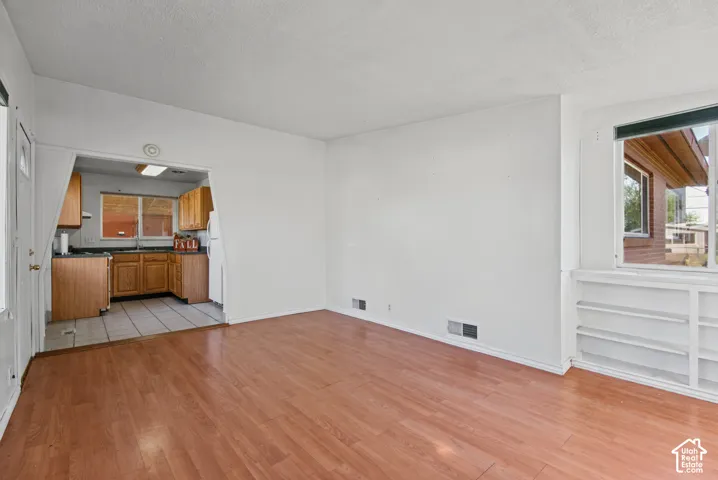 Living area featuring wood-finish flooring, built-in shelving, and a large window, with tile flooring visible in the kitchen