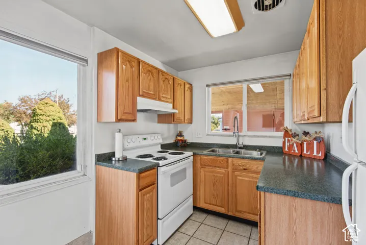 Kitchen featuring stained wood cabinetry, laminate countertops, a dual-basin stainless steel sink with a goose-neck faucet, and ceramic tile flooring