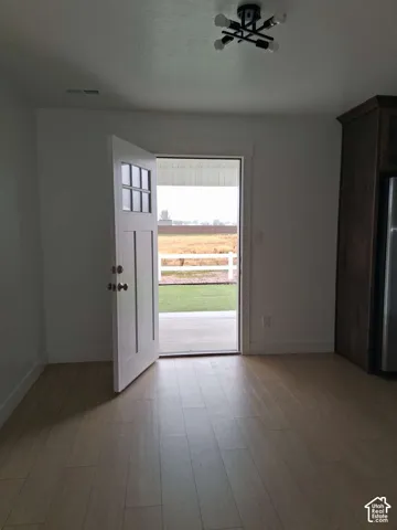 Wood-finish flooring, six-light modern geometric ceiling fixture, and white craftsman-style door with glass pane detail opening to a covered patio and railed yard area