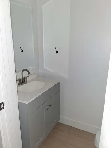 Grey vanity featuring a white countertop with an integrated basin, brushed nickel faucet, wall-mounted mirror, and wood-finish flooring
