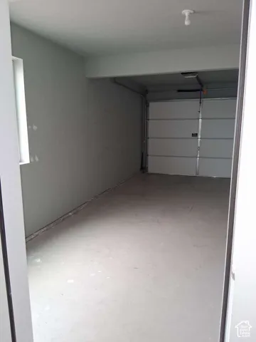 Garage interior featuring smooth-finished concrete flooring, painted walls, a white paneled overhead door, and a single ceiling-mounted light fixture