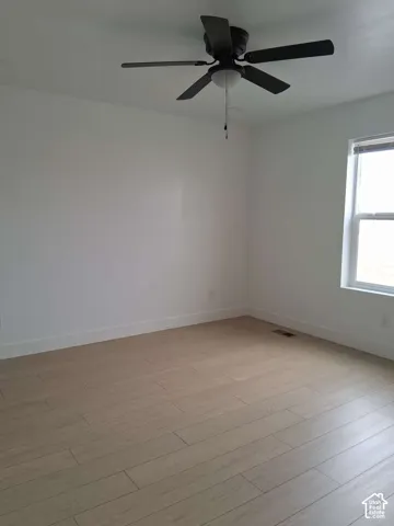 Interior room featuring light-toned wood-finish flooring, a multi-blade ceiling fan with integrated lighting, and a window with horizontal blinds