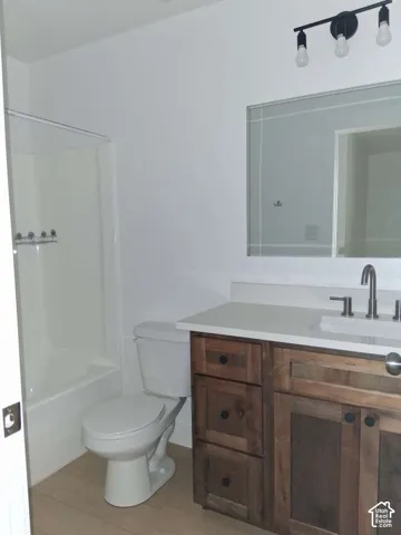 Bathroom featuring a vanity with wood-finish cabinetry, a white countertop, a rectangular undermount sink, a rectangular wall-mounted mirror, and a tub-shower combination