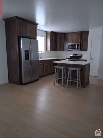 Kitchen featuring dark-toned cabinetry, a center island with a quartz countertop, stainless steel appliances, and wood-finish flooring