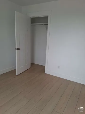 Room interior featuring wood-finish flooring, a multi-panel door, and a built-in closet with an integrated garment rod