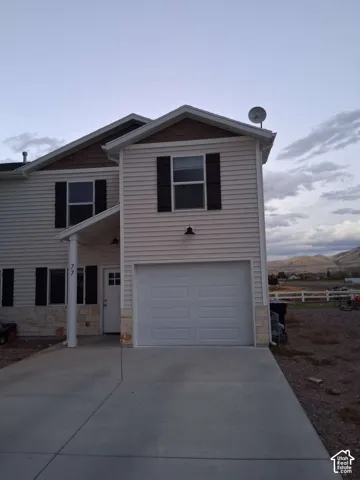Two-story exterior featuring light-colored horizontal siding, stone veneer accents, contrasting dark window shutters, a single-car garage, and a covered front entry