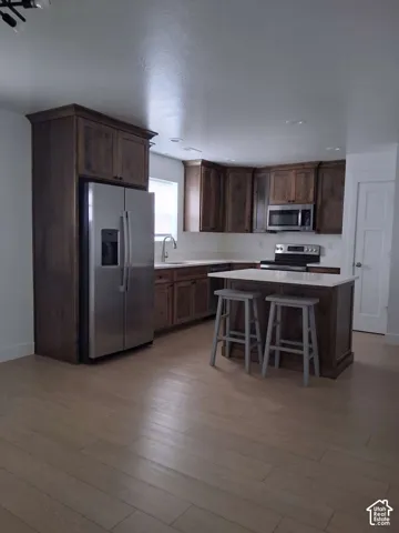 Kitchen featuring dark-stained cabinetry, a central island with a stone-surface countertop, stainless steel appliances, and wood-finish flooring