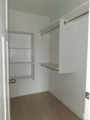 Walk-in closet featuring white built-in shelving, dual hanging rods, and wood-finish flooring