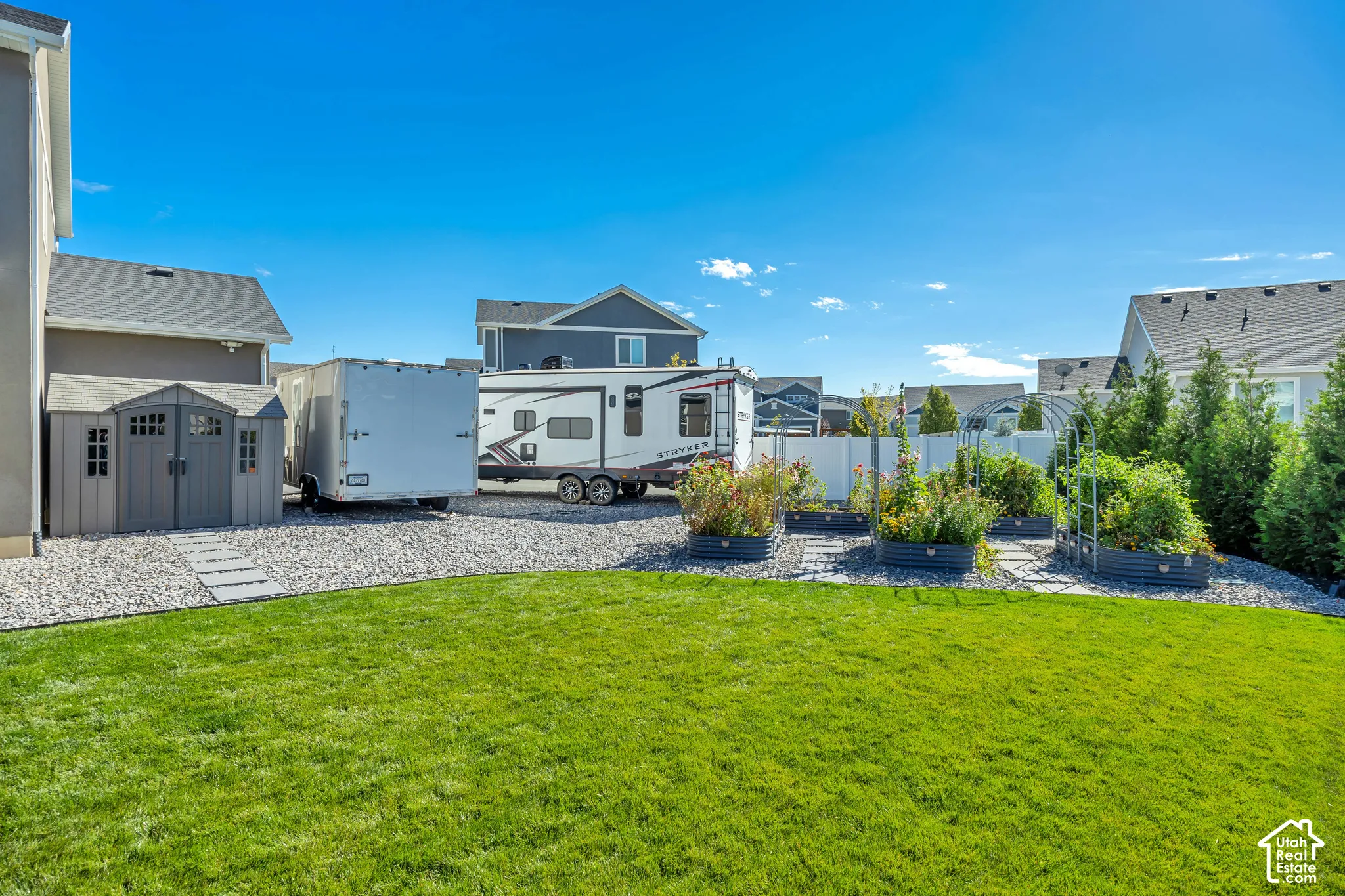Backyard featuring a manicured lawn, gravel-surfaced RV parking area, stone-finish garden beds, an enclosed storage structure, and privacy fencing