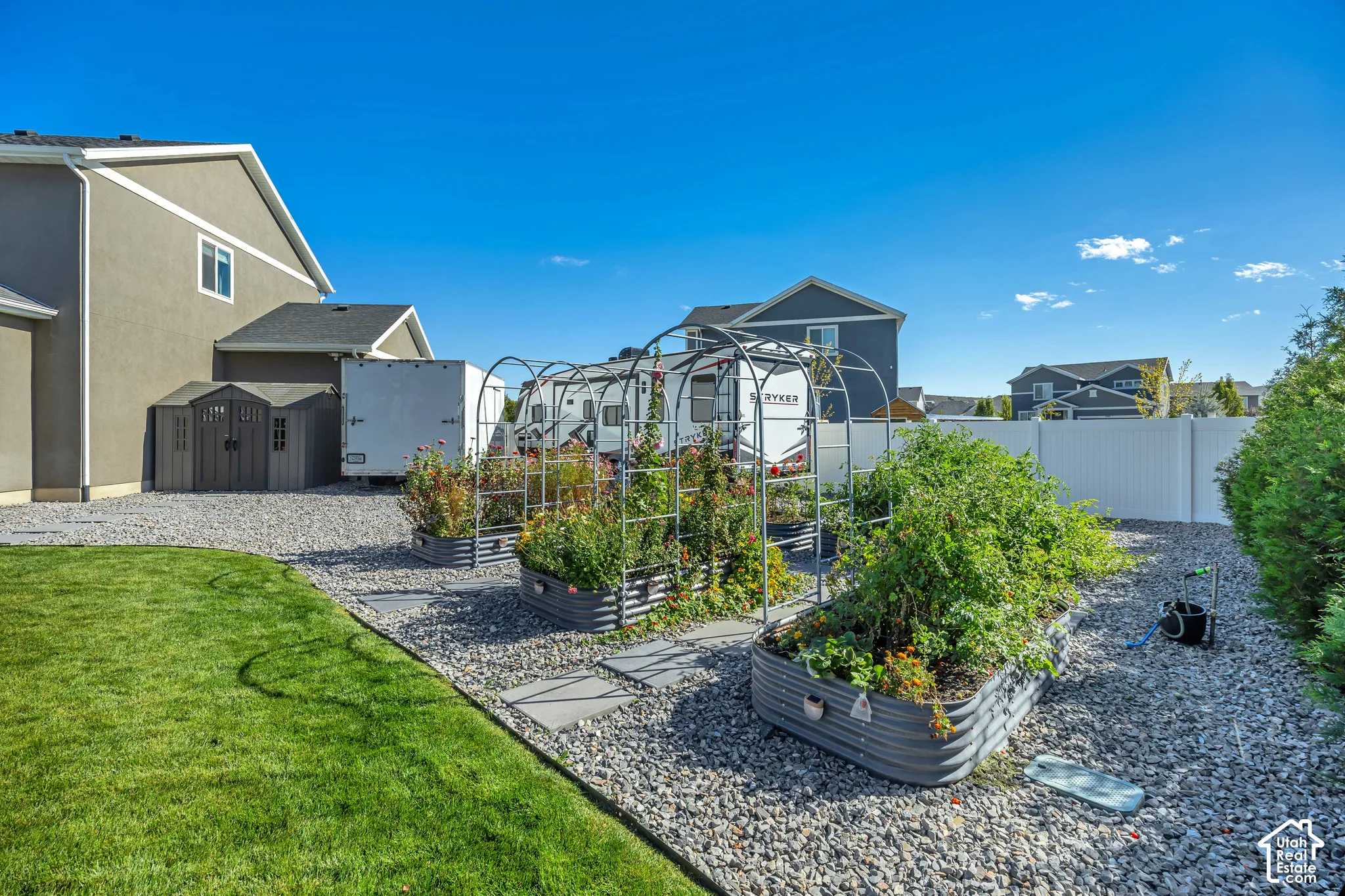 Backyard featuring a manicured lawn, multiple elevated garden beds with metal trellis arches, a stone-aggregate ground cover, and a resin storage shed