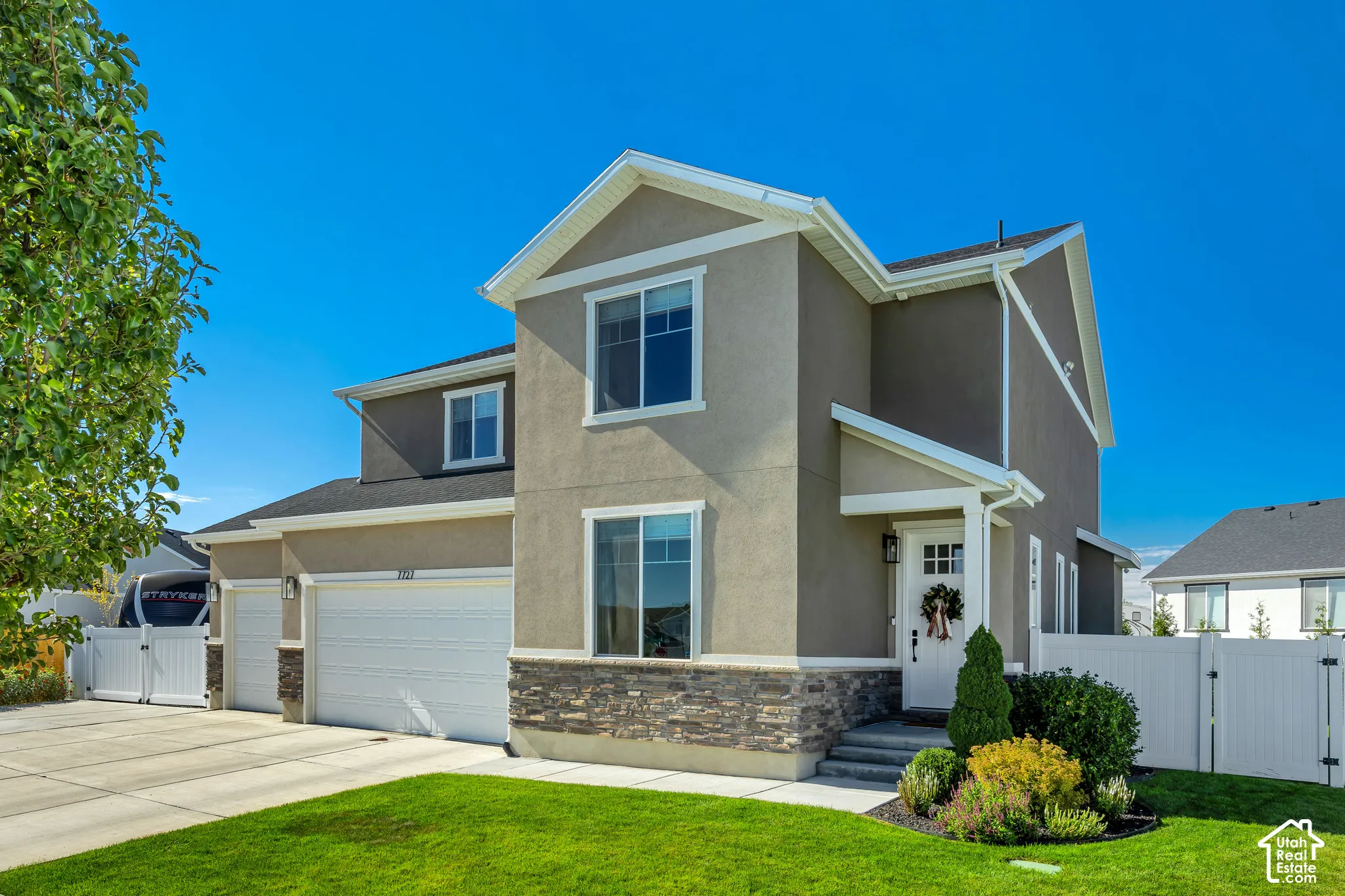 Two-story exterior featuring a stone veneer foundation, neutral stucco siding, a multi-paneled white front door, and a three-car garage