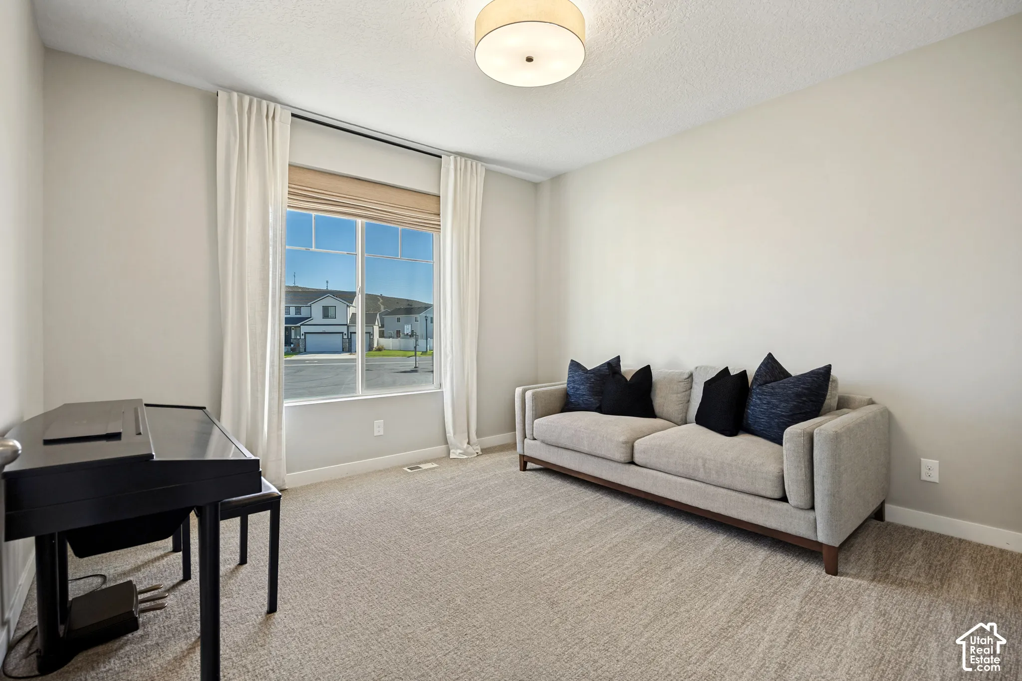 Neutral-toned room featuring textured carpeting, large window with natural lighting, and a modern drum-style flush mount ceiling light fixture