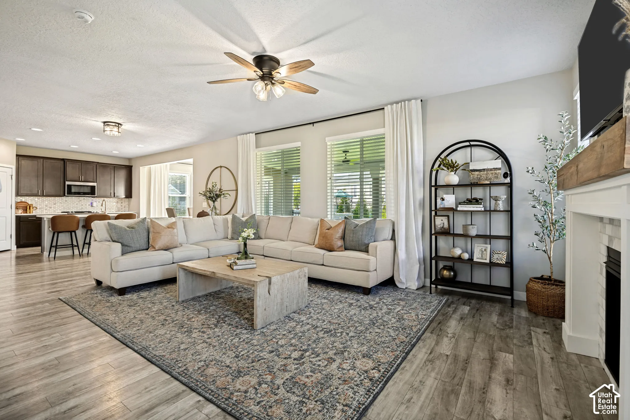 Open-concept living area featuring wood-finish flooring, a fireplace with a wood mantel and tile surround, ceiling fan, and recessed lighting