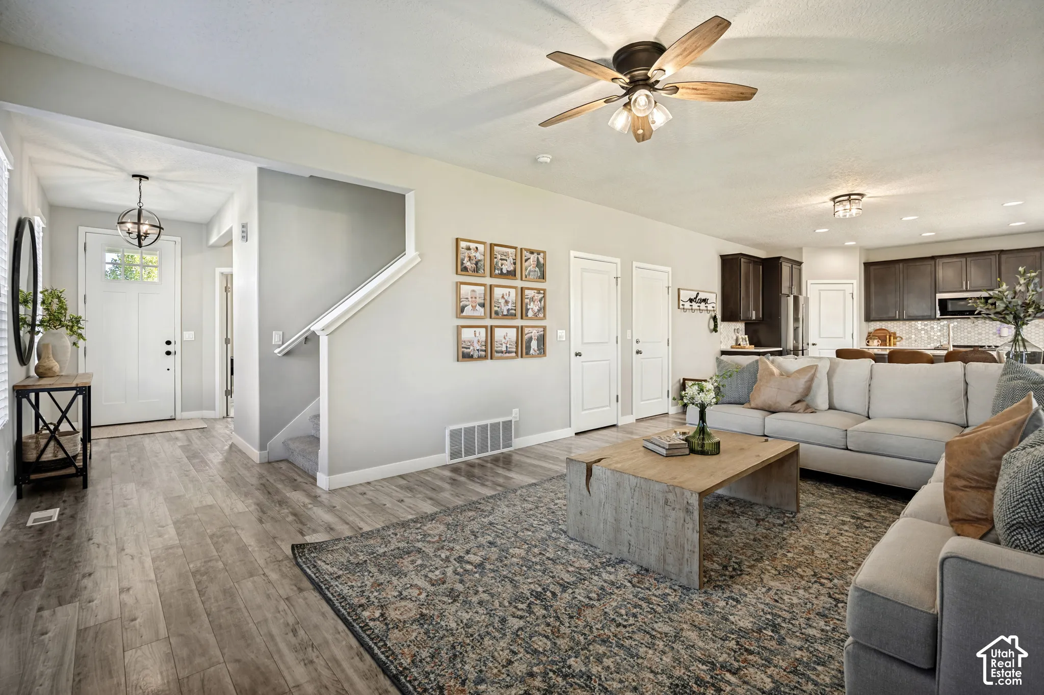 Open-concept interior featuring wood-finish flooring, a ceiling fan with integrated lighting, a globe-style entryway chandelier, and recessed ceiling lighting