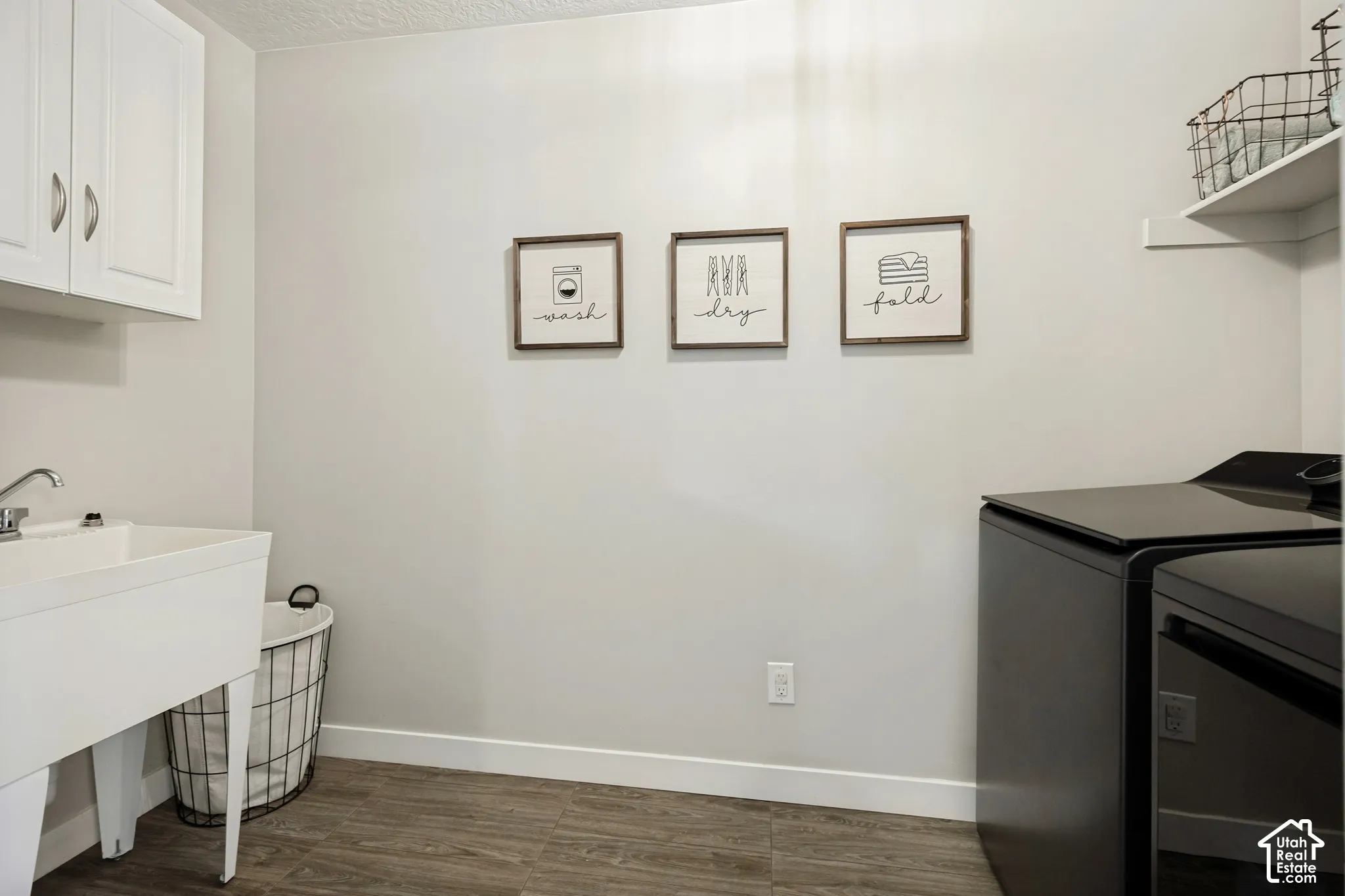 Laundry room featuring wood-finish flooring, white wall-mounted cabinetry, a utility sink, and open wall shelving