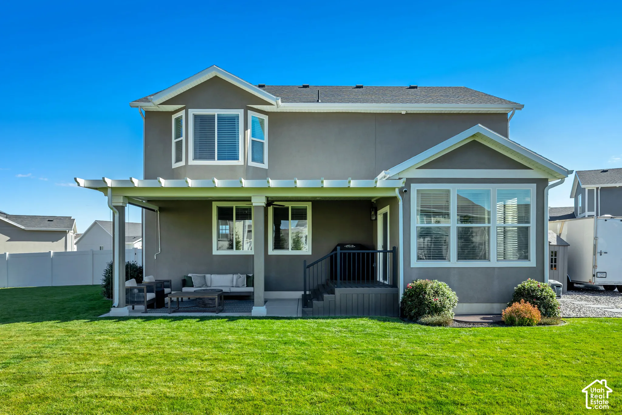 Two-story exterior featuring a covered pergola patio, manicured lawn, bay window, and exterior stairs with a metal railing