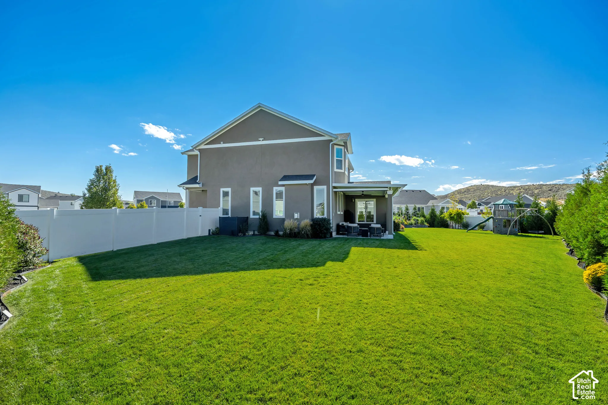 Expansive backyard featuring a manicured lawn, full-height perimeter vinyl fencing, and a covered rear patio