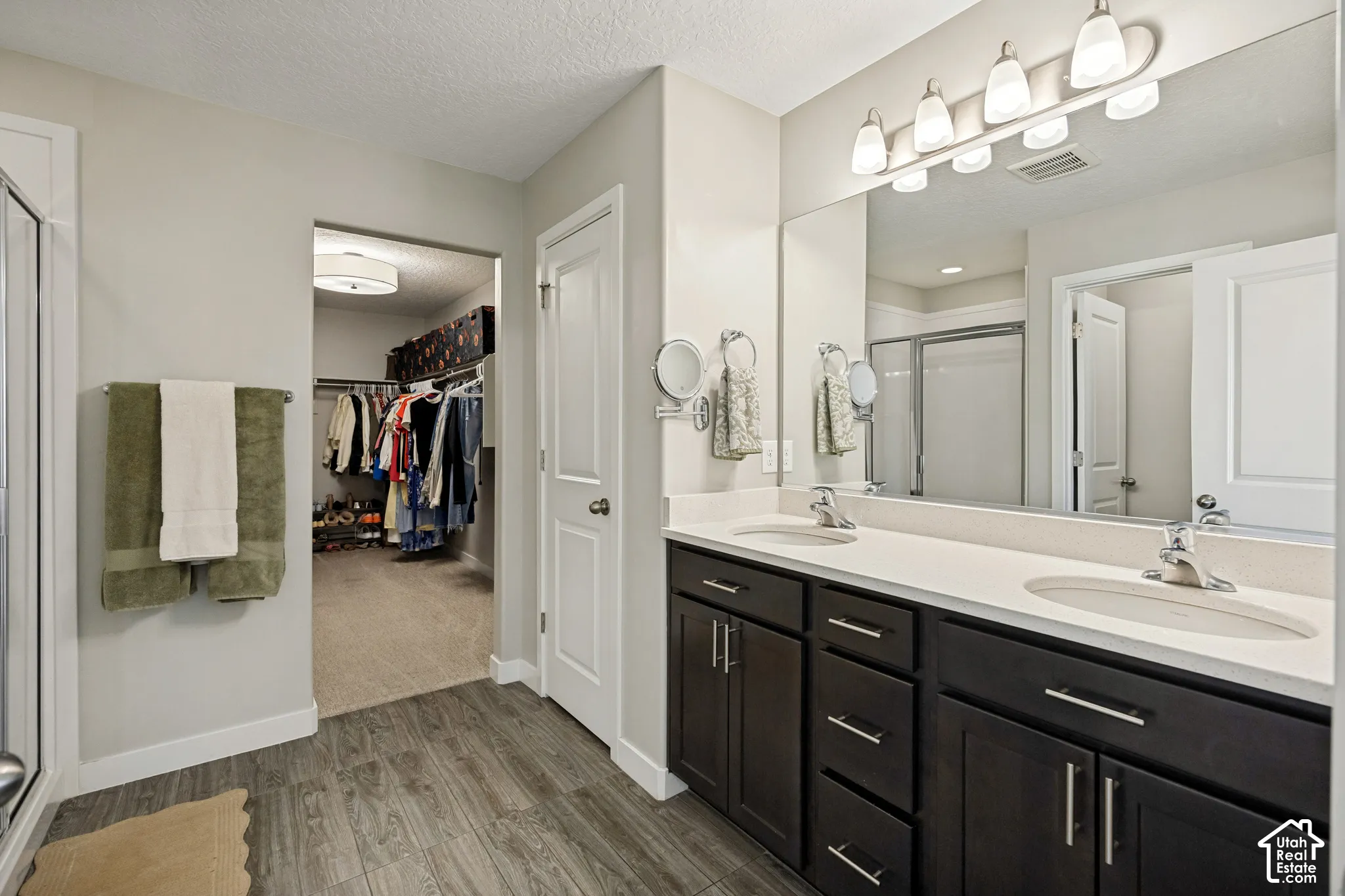 Dual-sink vanity with dark-finish cabinetry, solid-surface countertop, five-light overhead fixture, and large wall-mounted mirror