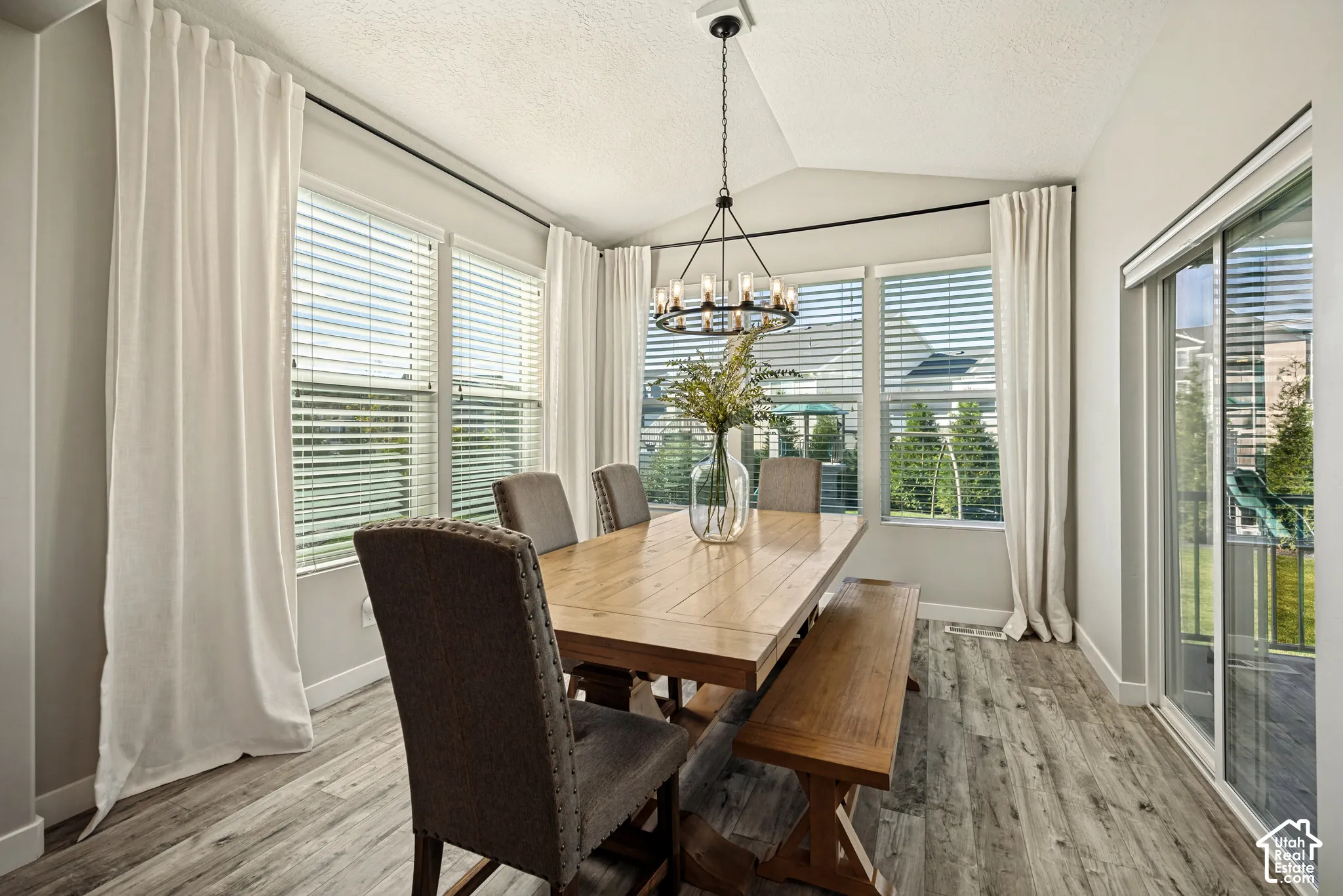 Vaulted ceiling dining area featuring wood-finish flooring, multi-pane windows, sliding glass door, and a circular chandelier