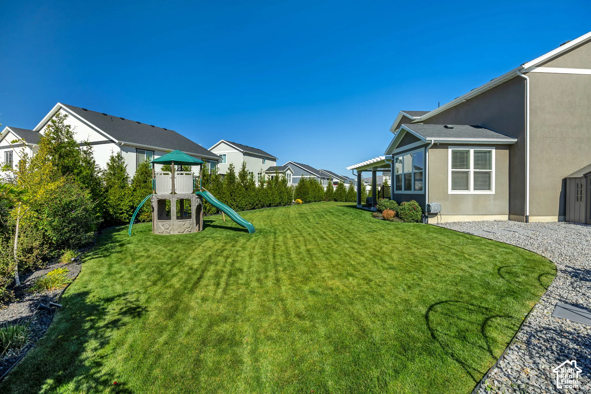 Expansive backyard featuring a manicured lawn, gravel perimeter, and a privacy hedge of mature evergreens