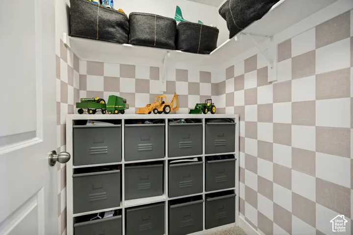 Storage area featuring built-in white shelving, checkered wall pattern, and white upper shelving
