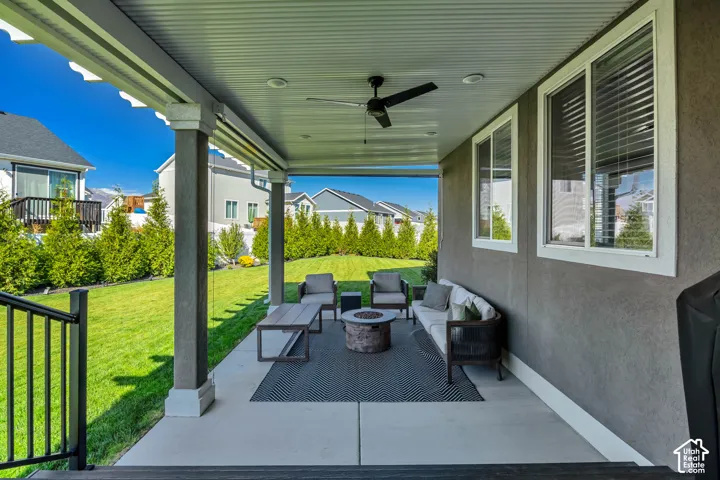 Covered patio featuring concrete flooring, a ceiling fan, recessed lighting, and square support columns, overlooking a manicured lawn with mature privacy hedging