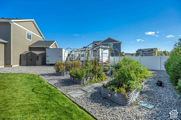 Backyard featuring a manicured lawn, multiple elevated garden beds with metal trellis arches, a stone-aggregate ground cover, and a resin storage shed
