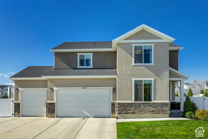 Two-story exterior featuring a neutral stucco finish, stone veneer accents, an asphalt shingle roof, and a three-car garage