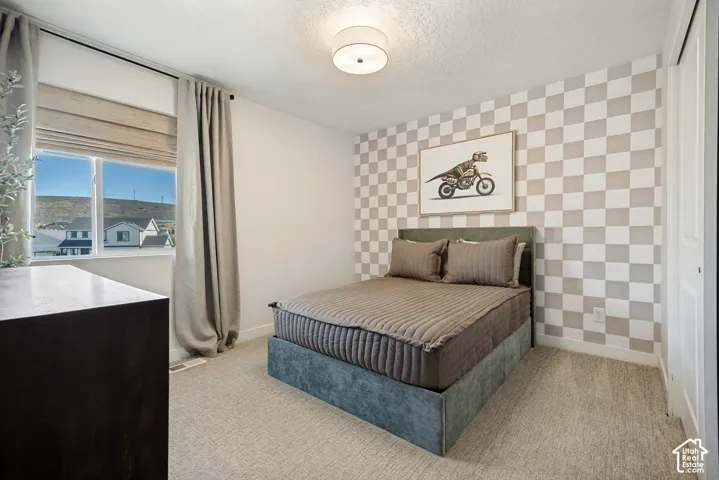 Bedroom featuring neutral wall-to-wall carpeting, checkered accent wall treatment, semi-flush mount drum lighting, and a single-hung window with a integrated roller shade