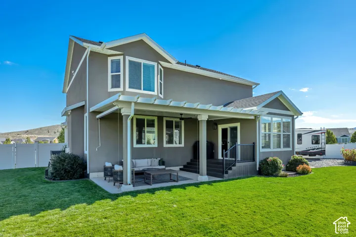 Two-story exterior with stucco siding, covered pergola patio, elevated deck with metal railing, and fenced backyard