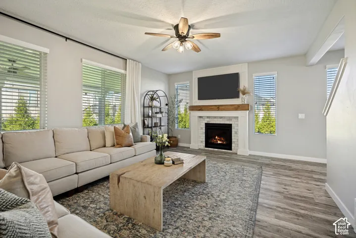 Living area featuring wood-finish flooring, a focal fireplace with a tile surround and natural wood mantel, and a multi-blade ceiling fan with integrated lighting