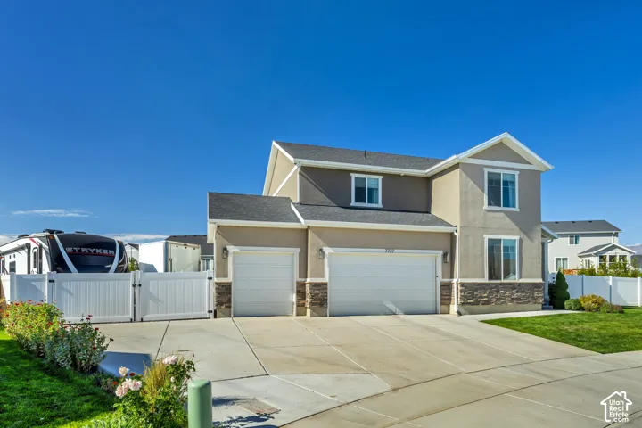 Two-story residence featuring a mixed stucco and stone veneer exterior, a three-car garage, a concrete driveway, and white vinyl privacy fencing