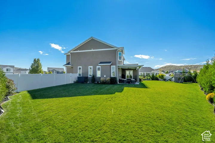 Expansive backyard featuring a manicured lawn, full-height perimeter vinyl fencing, and a covered rear patio