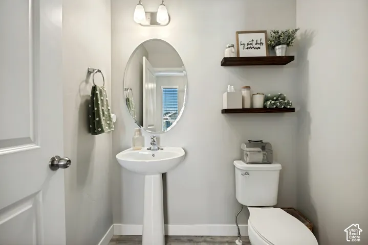 Pedestal sink with a polished chrome faucet, oval frameless mirror, dual-light vanity fixture, and two wood-finish floating shelves