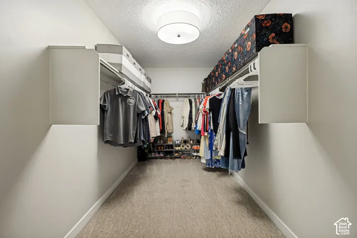 Walk-in closet featuring wall-to-wall carpeting, dual-tier built-in shelving, and a central drum-style ceiling light fixture