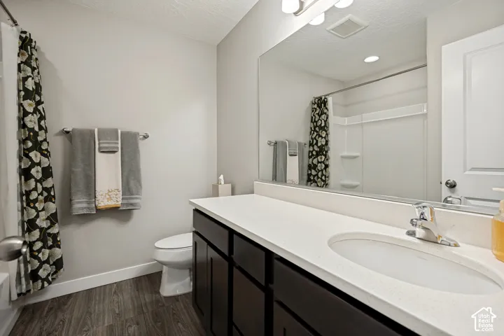 Bathroom featuring a dark-toned vanity cabinet with a solid surface countertop, an undermount oval sink, a large wall-spanning mirror, and wood-finish flooring