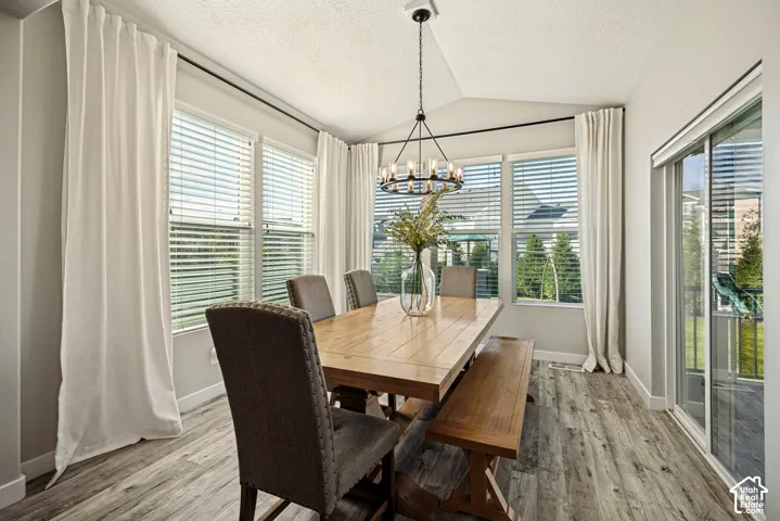 Vaulted ceiling dining area featuring wood-finish flooring, multi-pane windows, sliding glass door, and a circular chandelier