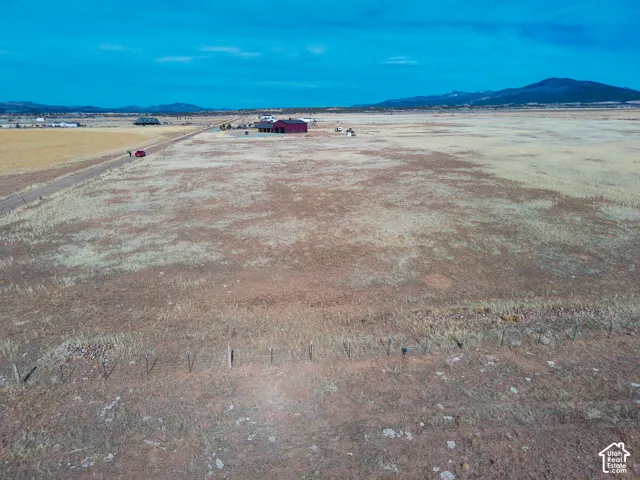 Expansive acreage featuring wire fencing, a red metal-sided barn, and a mountain backdrop
