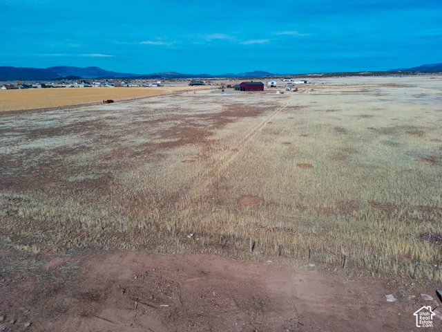 Expansive acreage featuring open terrain, wire perimeter fencing, a detached metal structure, and a mountain range backdrop