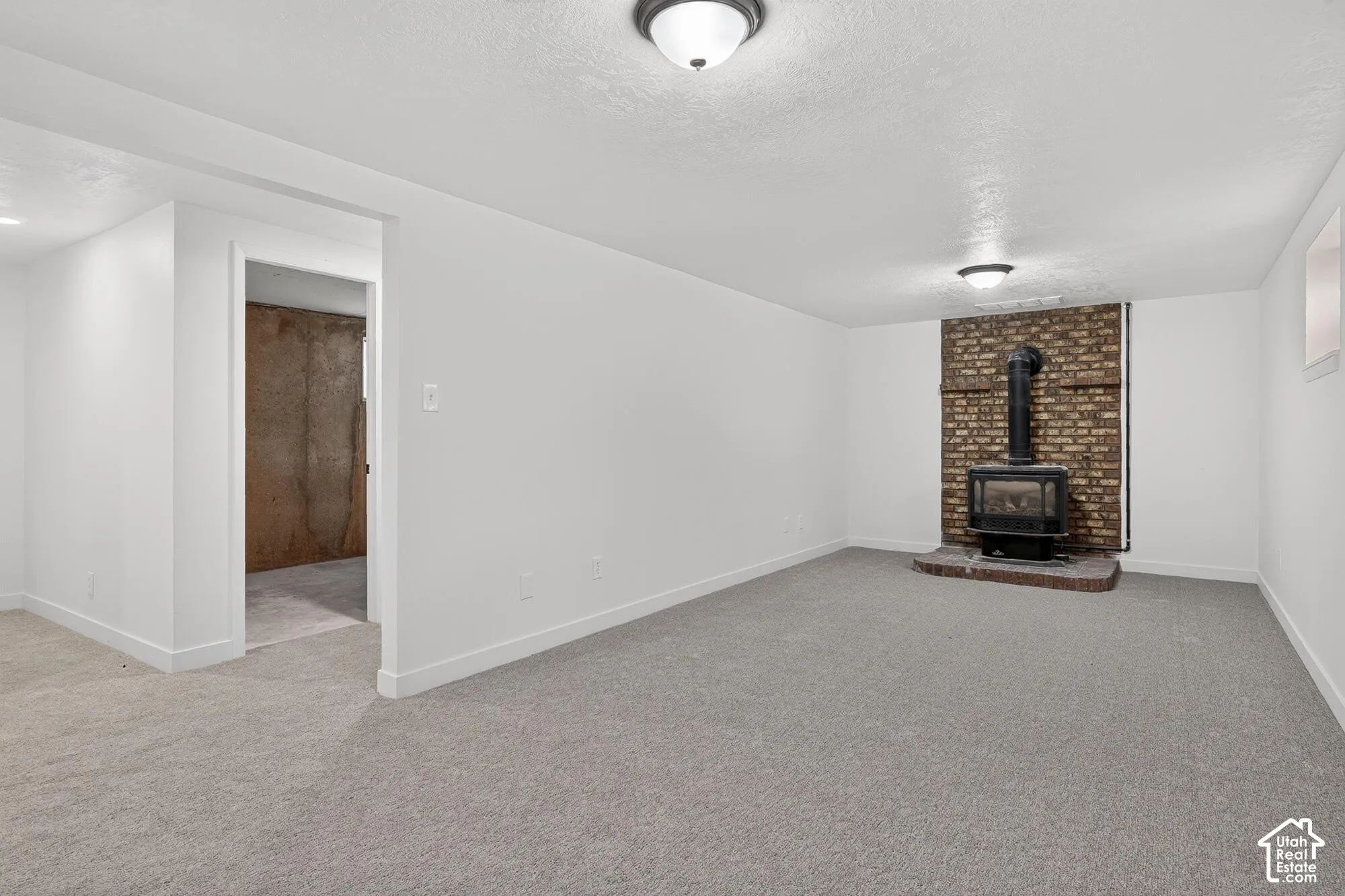 Interior space featuring neutral carpeting, a brick hearth, and a wood-burning stove with a metal chimney pipe