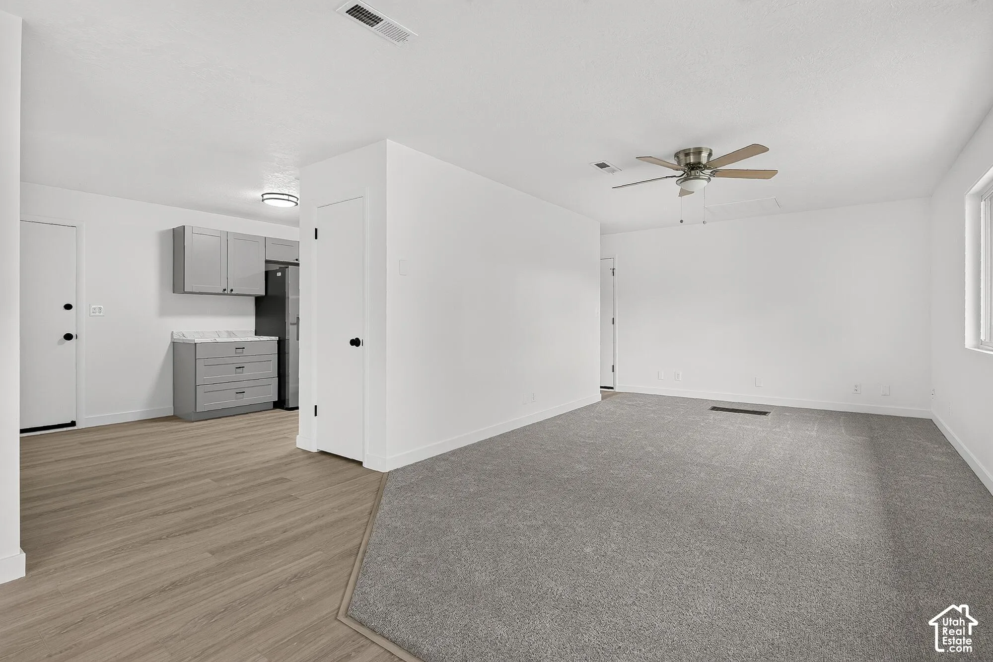 Interior space featuring wood-finish flooring, grey cabinetry with stone-finish countertops, neutral wall-to-wall carpeting, and a ceiling-mounted fan