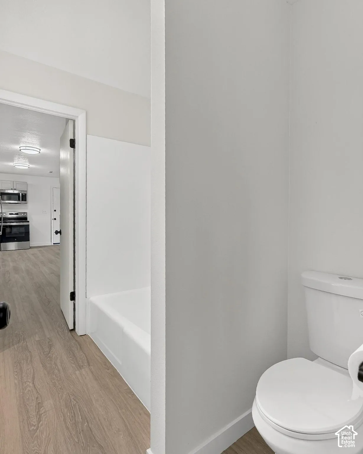 Bathroom featuring a white porcelain toilet and a tub-shower combination with a molded surround, finished with wood-finish flooring