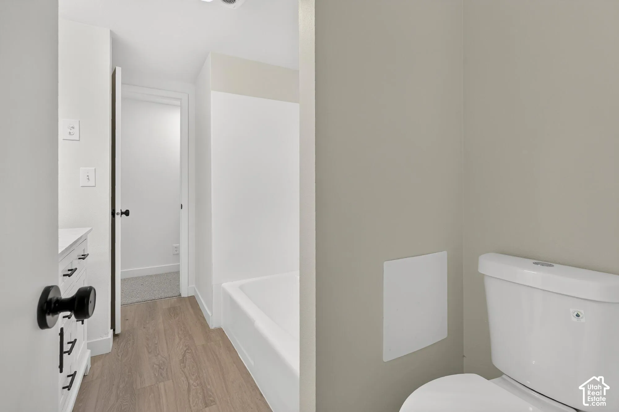 Bathroom featuring wood-finish flooring, white cabinetry with matte black hardware, and a tub-shower combination