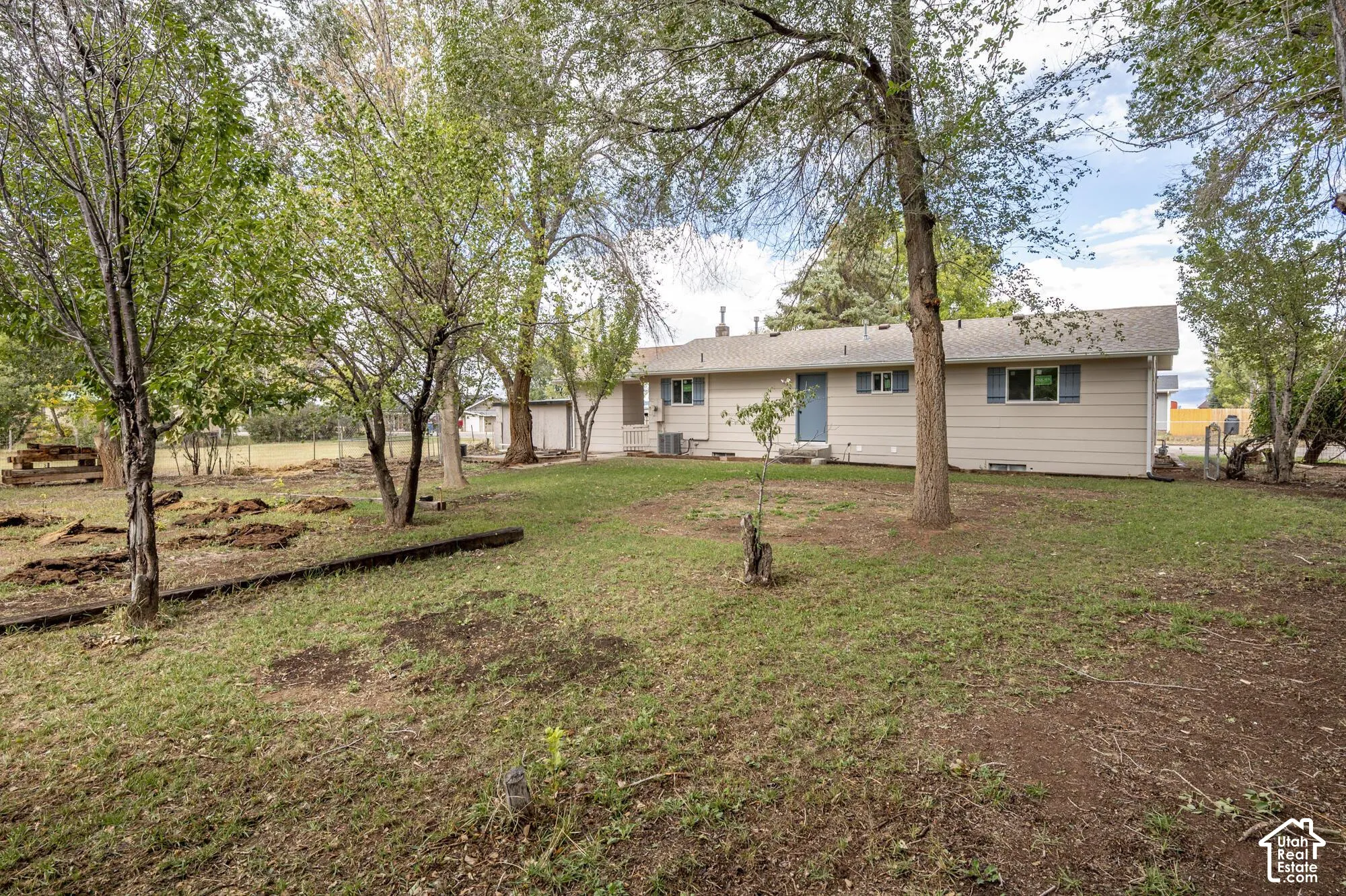 Expansive backyard featuring mature trees, horizontal lap siding, and a chain-link perimeter fence